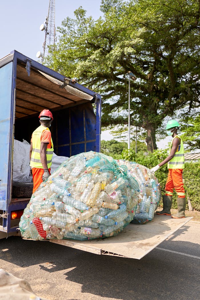 digital Two workers in protective gear loading plastic bottles onto a truck outdoors.